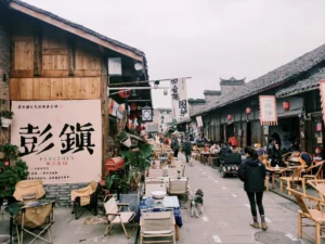 Pengzhen Old Street near Chengdu, with wooden shopfronts, tiled roofs, red lanterns and people drinking tea in bamboo chairs.