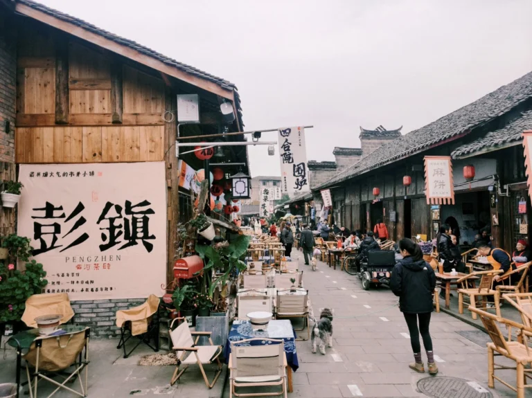 Pengzhen Old Street near Chengdu, with wooden shopfronts, tiled roofs, red lanterns and people drinking tea in bamboo chairs.
